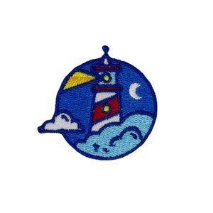 May include: A blue and white embroidered patch with a lighthouse, a crescent moon, and a cloud. The lighthouse has a red stripe and a yellow light beam.