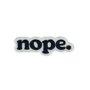 Puede incluir: Parche bordado con la palabra "nope" en negro, delineado con costuras blancas. El parche tiene un borde blanco y está sobre un fondo blanco. El parche es de forma rectangular.