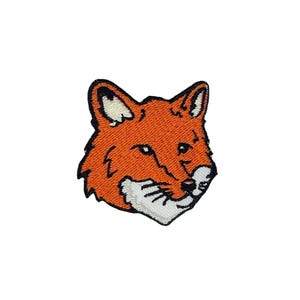 May include: Embroidered patch featuring a stylized fox head. The patch has an orange body with black outlines and white accents on the ears and muzzle. The fox has a friendly expression with black whiskers.