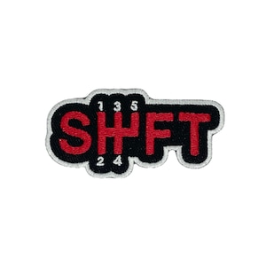 Op de afbeelding: Rode geborduurde patch met het woord "SHIFT" in witte omrande letters op een zwarte achtergrond. De nummers 1, 2, 3, 4 en 5 zijn geborduurd in wit op de patch.