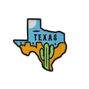 Op de afbeelding: Een geborduurde patch in de vorm van de staat Texas met een blauwe lucht, een oranje woestijn en een groene cactus. Het woord "TEXAS" staat in het zwart bovenaan de patch.