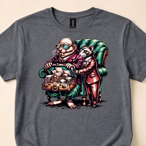 May include: A dark gray t-shirt featuring a graphic illustration of a mole in a suit and glasses sitting in a green armchair, holding an open briefcase filled with papers and gold, while a raccoon in a suit stands beside the chair.