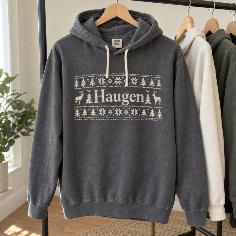 Charcoal hoodie on a clothing rail with Haugen lettering and a cream Nordic holiday design.