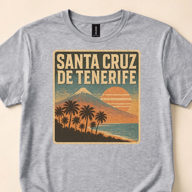 Close-up of a gray T-shirt with Santa Cruz de Tenerife lettering over palm trees, a coastal mountain and orange sunset.