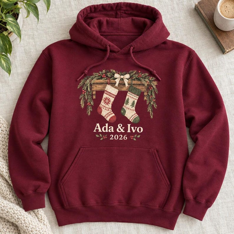 Burgundy hoodie with two Christmas stockings on a pine garland and Ada & Ivo 2026, flat lay