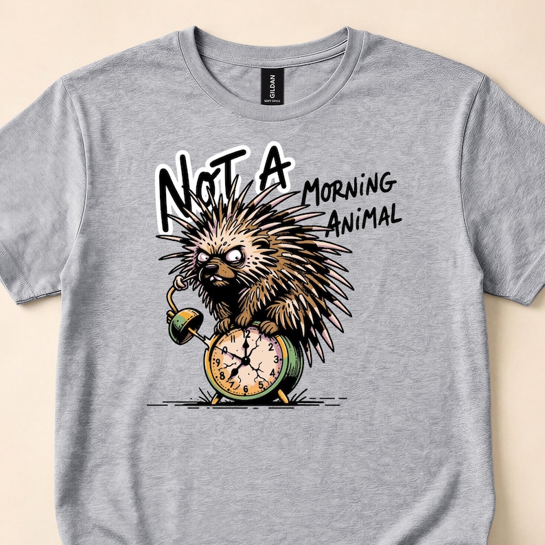 Gray T-shirt close-up with a spiky animal with a green mug and alarm clock beneath Not a Morning Animal lettering.