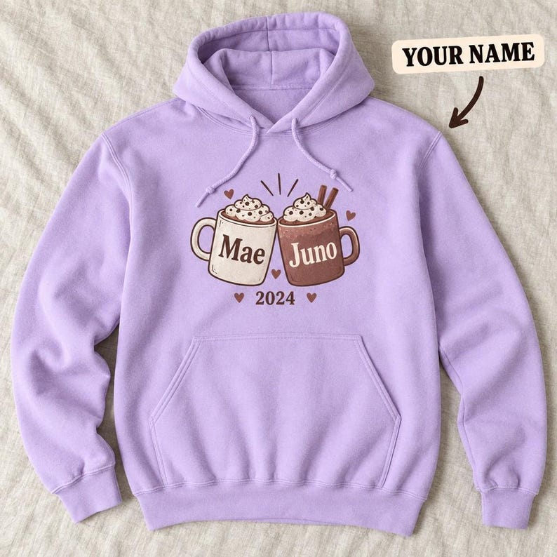 Lavender hoodie laid flat with two personalized cocoa mugs, hearts and a year.