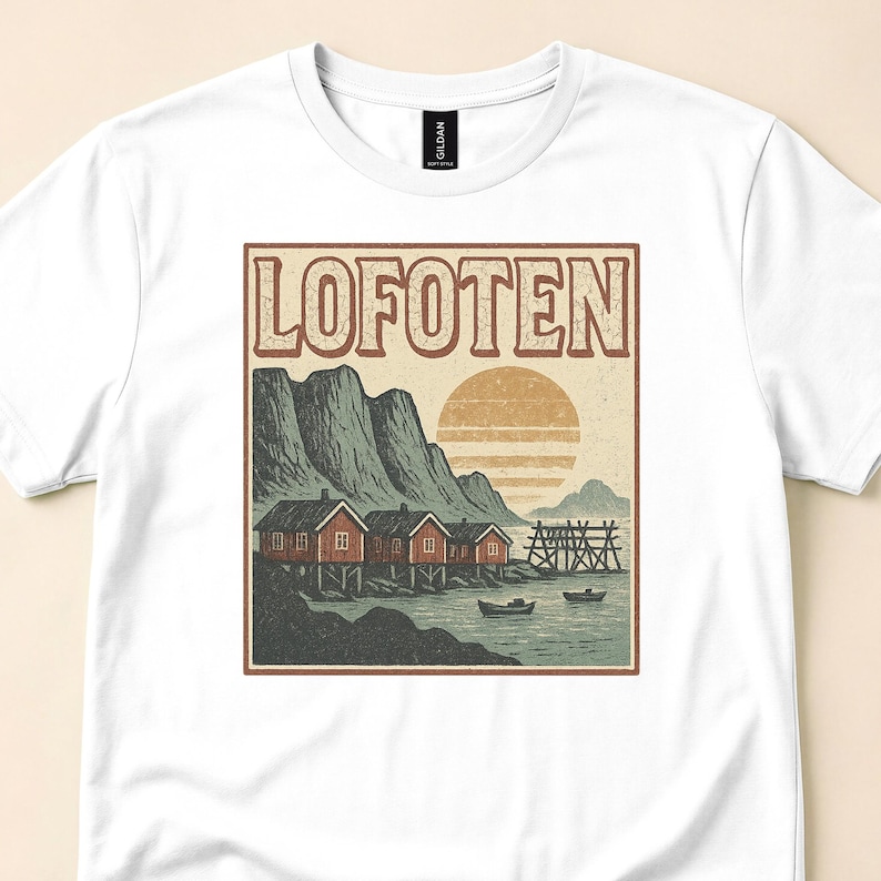 Close view of a white T-shirt with a "Lofoten" print showing red waterfront cabins, mountains, boats, and a striped sun.