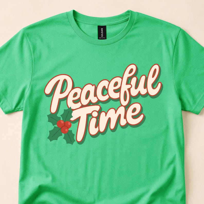 Close-up of a green T-shirt with cream Peaceful Time script beside green holly leaves and red berries.