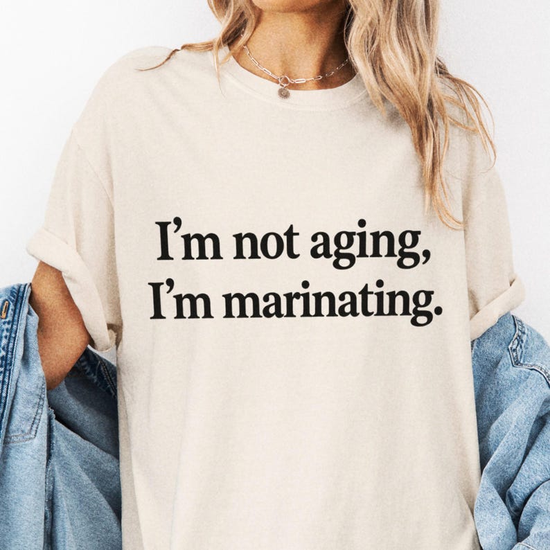 Cream T-shirt close-up on a wearer with black I'm Not Aging, I'm Marinating lettering.