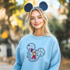 a woman wearing a blue sweatshirt with mickey mouse ears on her head