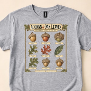 May include: A heather gray t-shirt featuring a botanical illustration titled ACORNS & OAK LEAVES. The graphic displays various acorns and oak leaves with labels including White Oak, Red Oak, Bur Oak, Pin Oak, Black Oak, Live Oak, Water Oak, Chestnut Oak, and Post Oak.