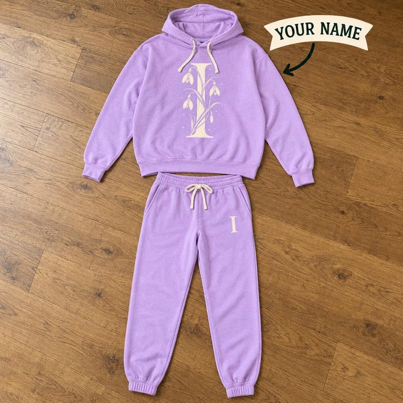Violet hoodie with a cream initial I wrapped in snowdrop flowers and matching joggers laid flat on wood