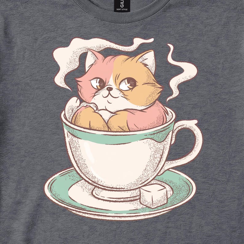Charcoal tee close-up showing an orange-and-pink cat sitting in a steaming teacup on a saucer.