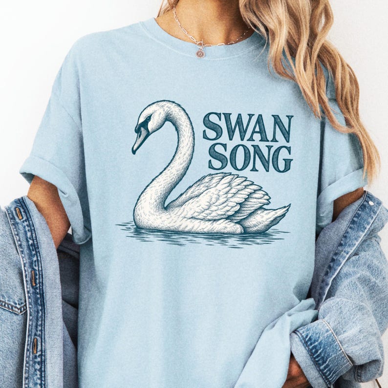 Close view of a model in a pale blue tee with an illustrated white swan on water and dark Swan Song lettering.