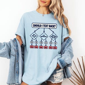 May include: A light blue t-shirt featuring a dark blue graphic flowchart titled SHOULD I TEXT BACK? with three decision diamonds asking DO I FEEL LIKE IT?, IS IT IMPORTANT?, and WILL IT MAKE THINGS BETTER?, all leading to red boxes labeled NO.