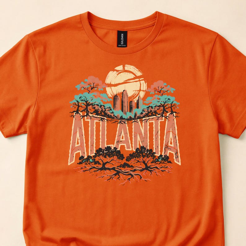 Close-up of an orange T-shirt with ATLANTA lettering, a skyline, sun and tree illustrations.