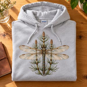May include: A light gray hooded sweatshirt featuring a graphic print of a dragonfly centered between two horsetail plants. The hoodie has a drawstring hood and a Gildan brand label on the inside neck area. The design displays detailed insect wings.