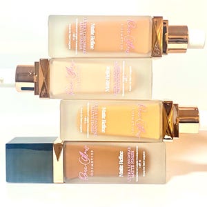 May include: Four bottles of Rose Glow Cosmetics Matte Refine Ultra Longwear Matte Finish foundation in various shades. The bottles are clear glass with gold accents and a pump dispenser.