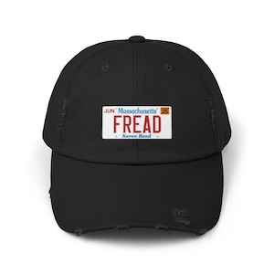 May include: Black distressed baseball cap with a license plate design. The license plate reads "FREAD" in red letters, with "Massachusetts" and "Karen Read" printed on it. The cap has a curved brim and a distressed look.