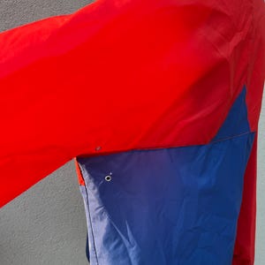 May include: A red and blue windbreaker jacket with a zipper closure. The jacket has a contrasting color design with a red upper section and a blue lower section.