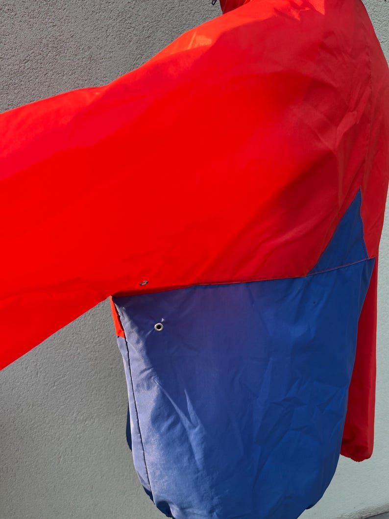 May include: A red and blue windbreaker jacket with a zipper closure. The jacket has a contrasting color design with a red upper section and a blue lower section.