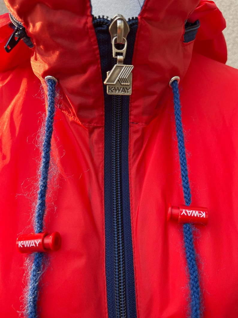 May include: Red hooded jacket with a navy blue zipper and K-Way branding on the zipper pull and the bottom of the jacket.