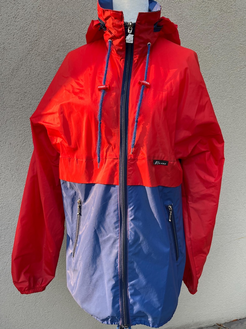 May include: A red and blue hooded jacket with a zipper closure and two pockets. The jacket has a logo on the left side of the chest.