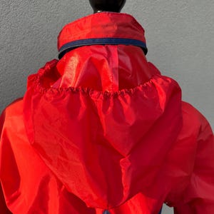 May include: Red and blue hooded jacket with a zipper closure. The jacket is made of a lightweight, water-resistant material.