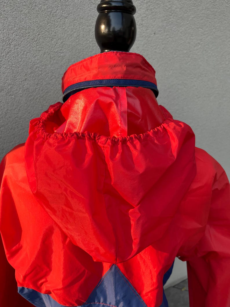 May include: Red and blue hooded jacket with a zipper closure. The jacket is made of a lightweight, water-resistant material.