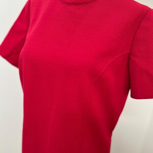 May include: A bright red dress with short sleeves and a round neckline. The dress has a textured, ribbed fabric and a tailored fit. The dress is displayed on a mannequin.