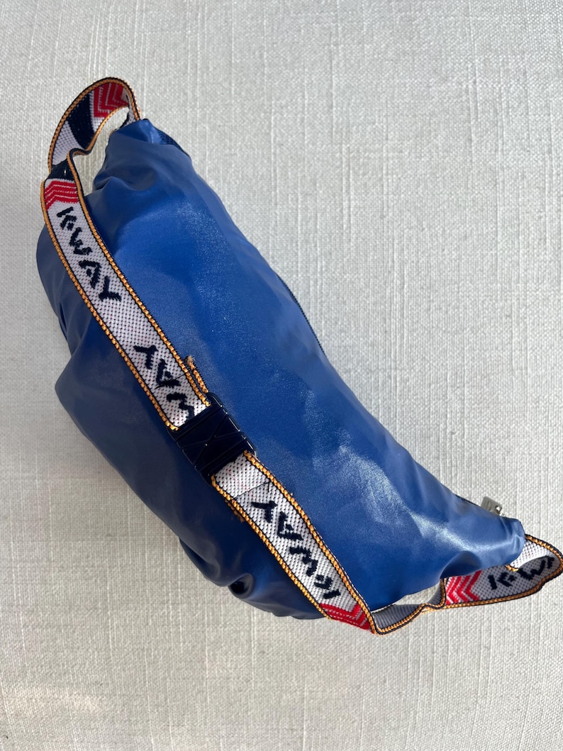 May include: A blue fanny pack with a white and red strap that says "AWAY" in white and yellow lettering.