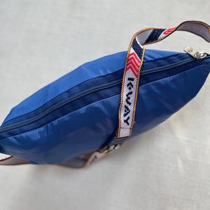 May include: A blue nylon drawstring bag with a zipper closure and a white and red striped strap with the text "I-WAY" printed on it.