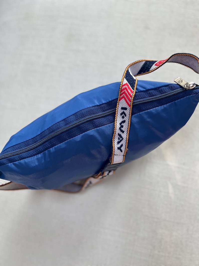May include: A blue nylon drawstring bag with a zipper closure and a white and red striped strap with the text "I-WAY" printed on it.