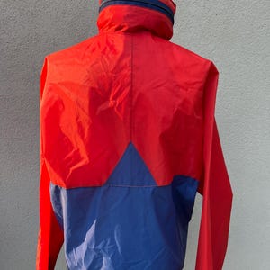 May include: A red and blue windbreaker jacket with a zipper closure. The jacket has a high collar and a contrasting color design.