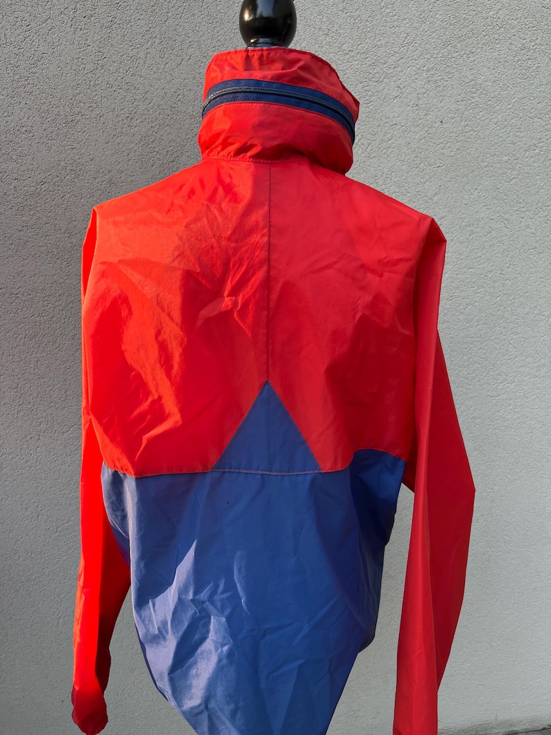 May include: A red and blue windbreaker jacket with a zipper closure. The jacket has a high collar and a contrasting color design.