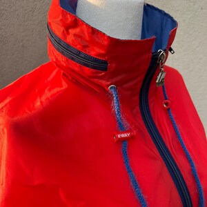 May include: Red hooded jacket with a blue lining and a zipper closure. The jacket has a K-Way logo on the front.