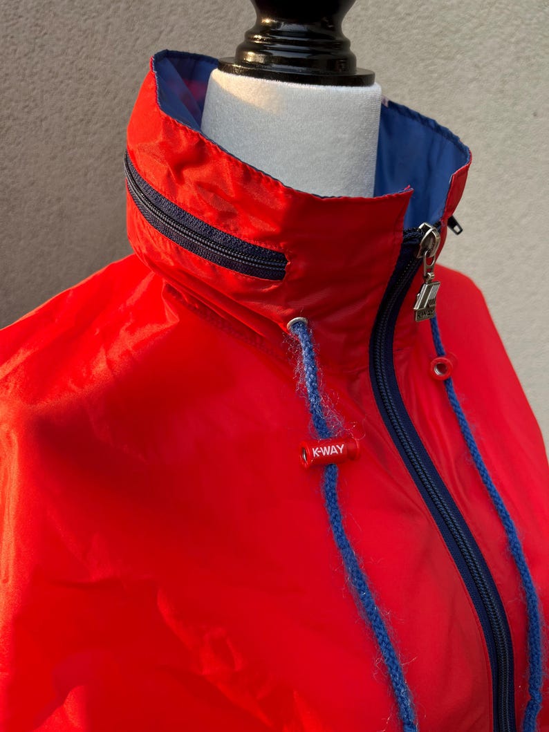 May include: Red hooded jacket with a blue lining and a zipper closure. The jacket has a K-Way logo on the front.