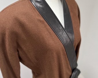 May include: A brown wrap dress with a black leather trim around the neckline and a black leather belt that ties at the waist.