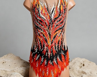 May include: A gymnastics leotard on a mannequin, featuring a fiery design in red, orange, and black, embellished with sparkling rhinestones. The leotard has a nude mesh overlay and is displayed with two large, textured stones.