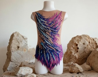 Puede incluir: Maillot beige con un diseño vibrante de plumas azules, moradas y rosas. La prenda sin mangas se exhibe en un maniquí blanco, mostrando el intrincado patrón. El maillot está diseñado para gimnasia o danza.