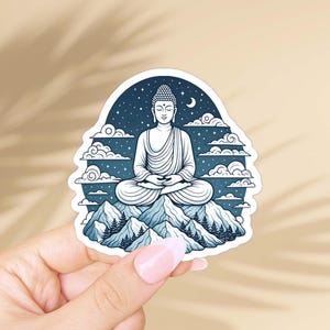 May include: A die-cut sticker featuring a dark blue illustration of a Buddha figure sitting in a meditative pose atop a mountain range. The scene includes stylized clouds, a crescent moon, and a starry night sky, all rendered in shades of blue.