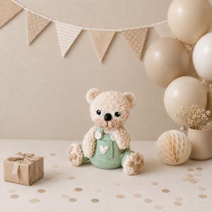 May include: A plush teddy bear with cream-coloured fuzzy fur, black eyes, and a black nose, wearing sage green overalls with a white heart detail on the front. The bear has tan paw pads and is sitting upright, featuring a soft, textured appearance.