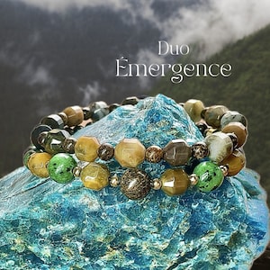 May include: Two beaded bracelets with a variety of earth-toned gemstones, including green, brown, and gold. The bracelets are displayed on a textured, turquoise-colored surface. The image includes text that reads "Collection Révélez-vous" and "Duo Émergence".