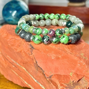 Può includere: Un braccialetto multifilo realizzato con perline di pietre preziose verdi e rosse con accenti argentati. Il braccialetto è su una superficie di roccia rossa.