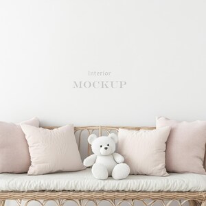 May include: A white wicker bench with a white teddy bear sitting in the middle. The bench has pink throw pillows on each end and a white throw pillow in the middle.