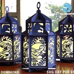 May include: Three dark blue paper lanterns with dinosaur cutouts. Each lantern has a handle and is decorated with a dinosaur silhouette. The lanterns are lit from within, creating a warm glow. The words "DIGITAL DOWNLOAD" are visible.