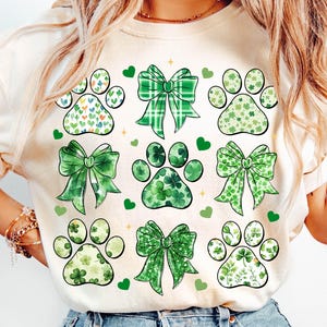 May include: Cream-colored sweatshirt featuring a St. Patrick's Day design. The design includes paw prints filled with hearts, clovers, and floral patterns, along with green bows and hearts. The overall theme is festive and pet-friendly.