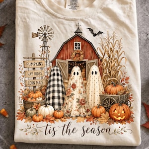 Op de afbeelding: Een crèmekleurig t-shirt met een afbeelding van een rode schuur, windmolen, maïs en drie geesten. De geesten hebben zwart-wit geblokte, bloemrijke en gestippelde patronen. De tekst luidt PUMPKINS, HAY RIDES, CORN MAZE en tis the season.