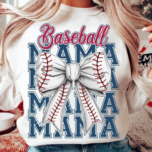 May include: White sweatshirt with a baseball-themed design. The design features the words "Baseball Mama" in red and blue, along with a large bow shaped like a baseball with red stitching. The word "MAMA" is repeated multiple times.